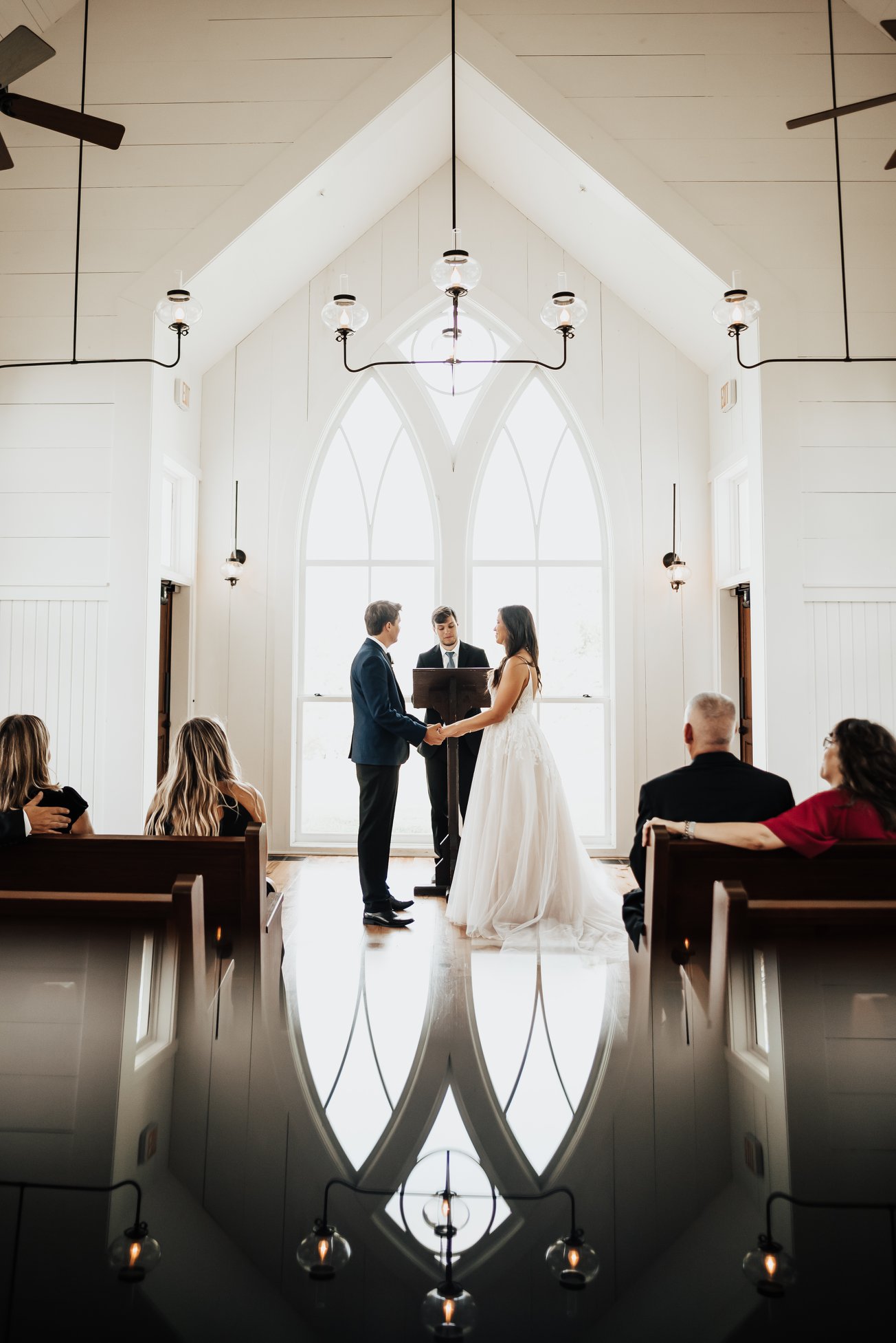 a wedding ceremony taking place in a chapel with a low number of guests