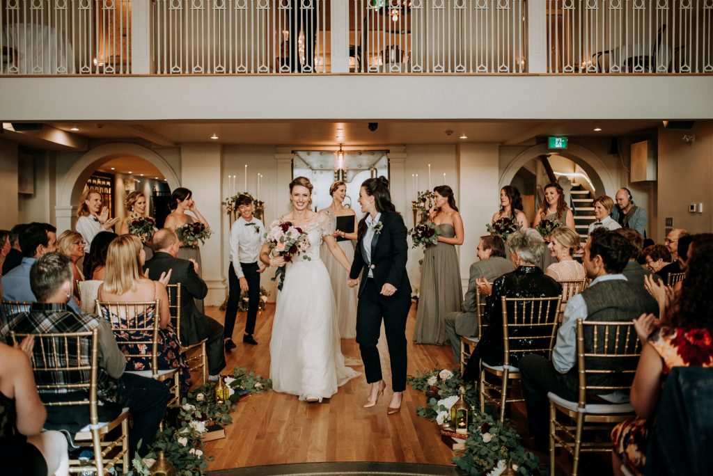 A wedding couple just got married and is walking back the aisle at the Permanent, one of the wedding venues Vancouver offers.