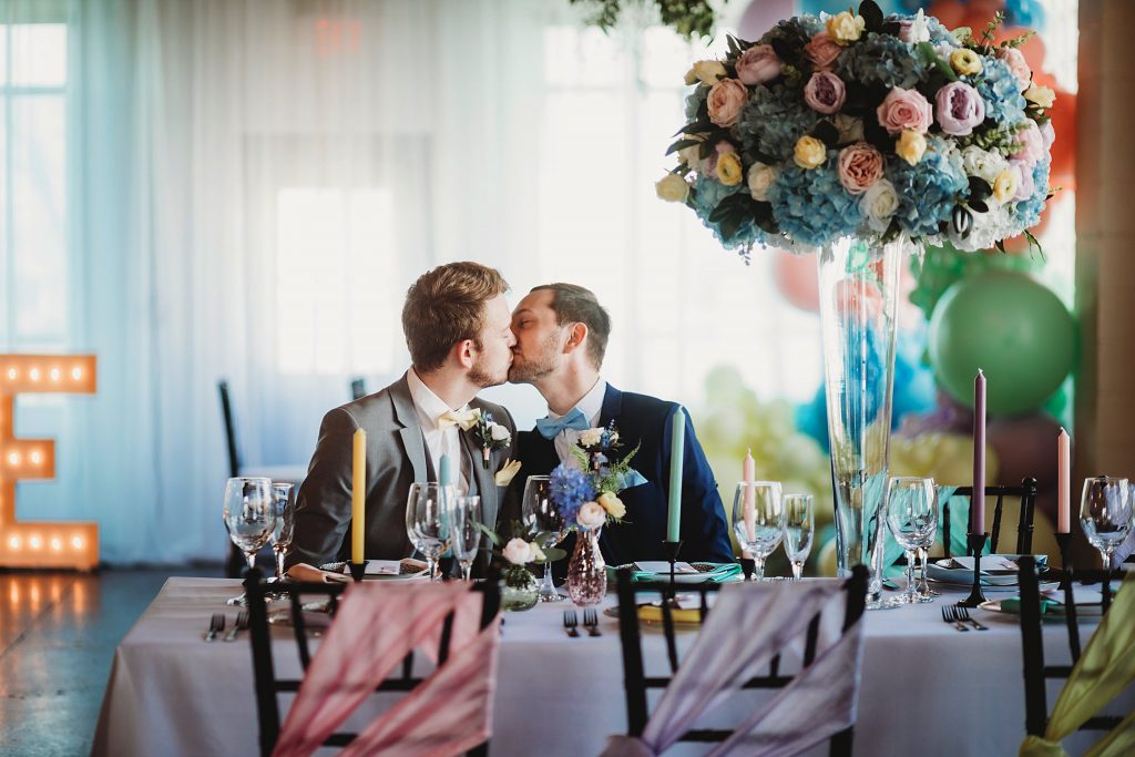 A wedding couple is sitting at the dining table and kissing each other at the Ivory Foundry, one of the wedding venues Indianapolis offers.