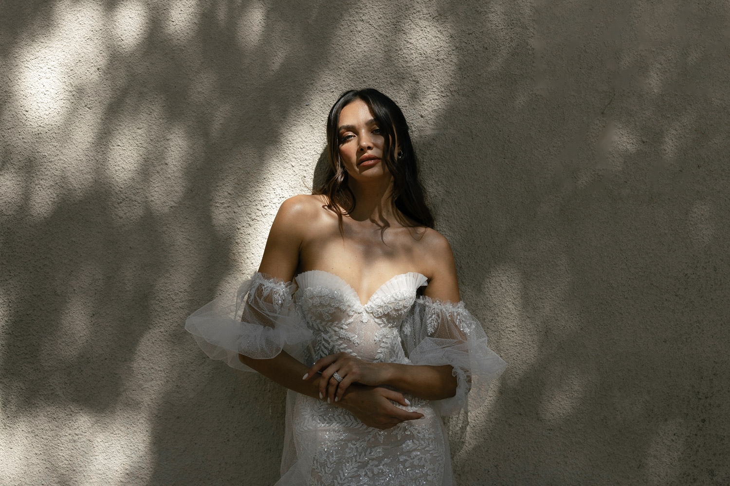 Bride bathed in dappled sunlight against a textured wall, her gaze exuding the serene beauty highlighted by Editorial Wedding Presets.