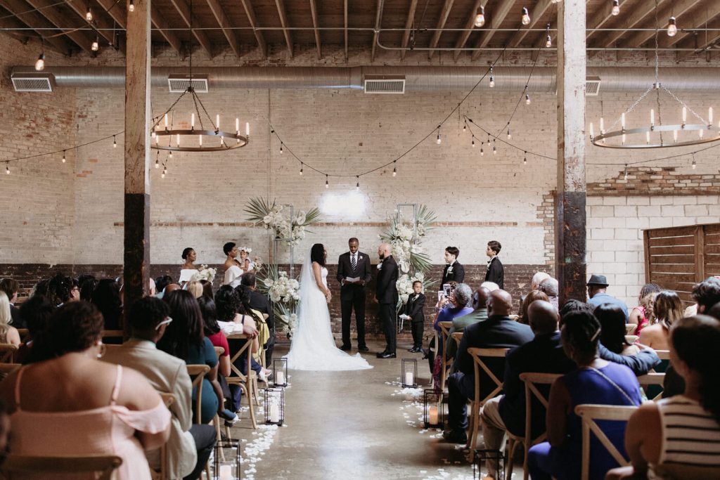A wedding couple is standing at the altar and is getting married, at the Brake and Clutch Warehouse, one of the Dallas wedding venues.