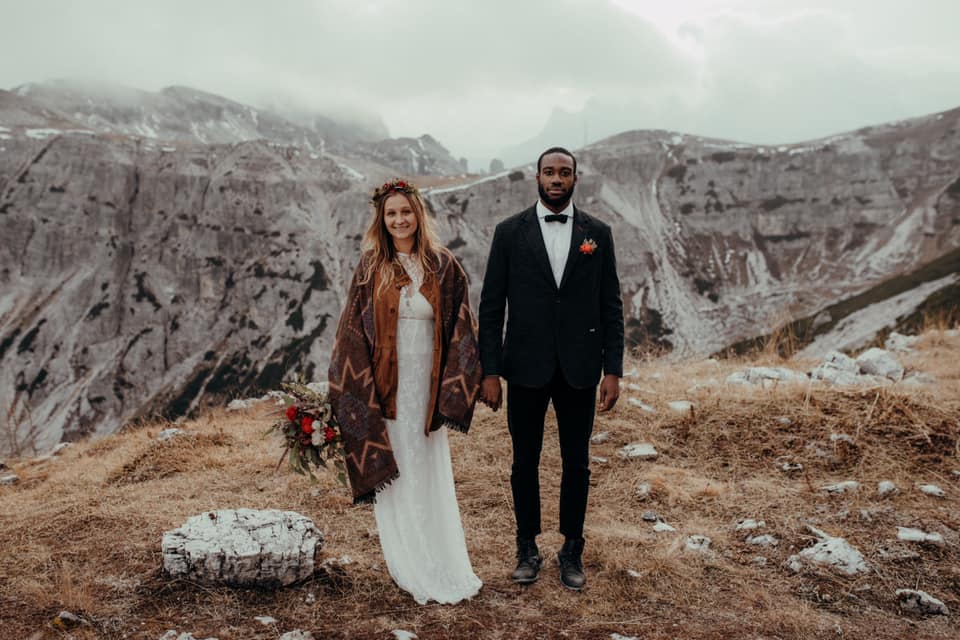 A wedding couple is holding hands and standing on top of a mountain in the Dolomites.