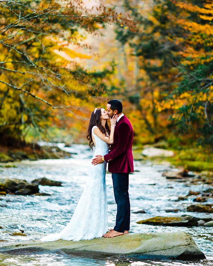 A wedding couple is kissing each other and standing on a flat rock in the middle of a lake at the Catskill Mountains.
