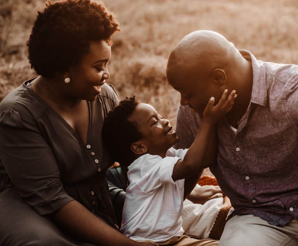 two adults and their son are sitting in a field and get their family pictures taken