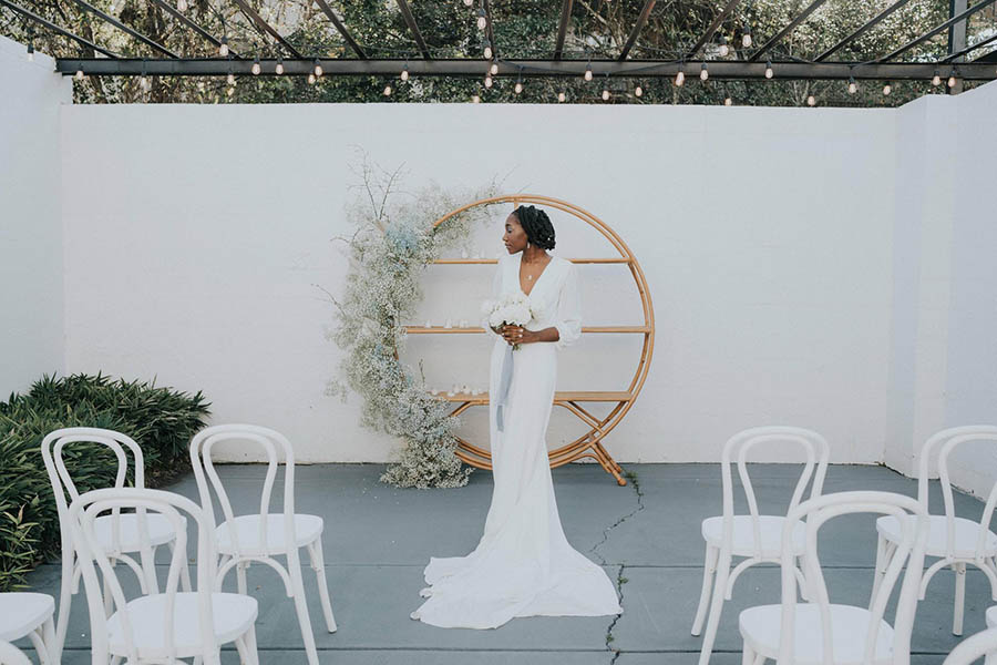 A bride is standing in front of a white wall and a wooden shelf at one of the best wedding venues in Georgia.