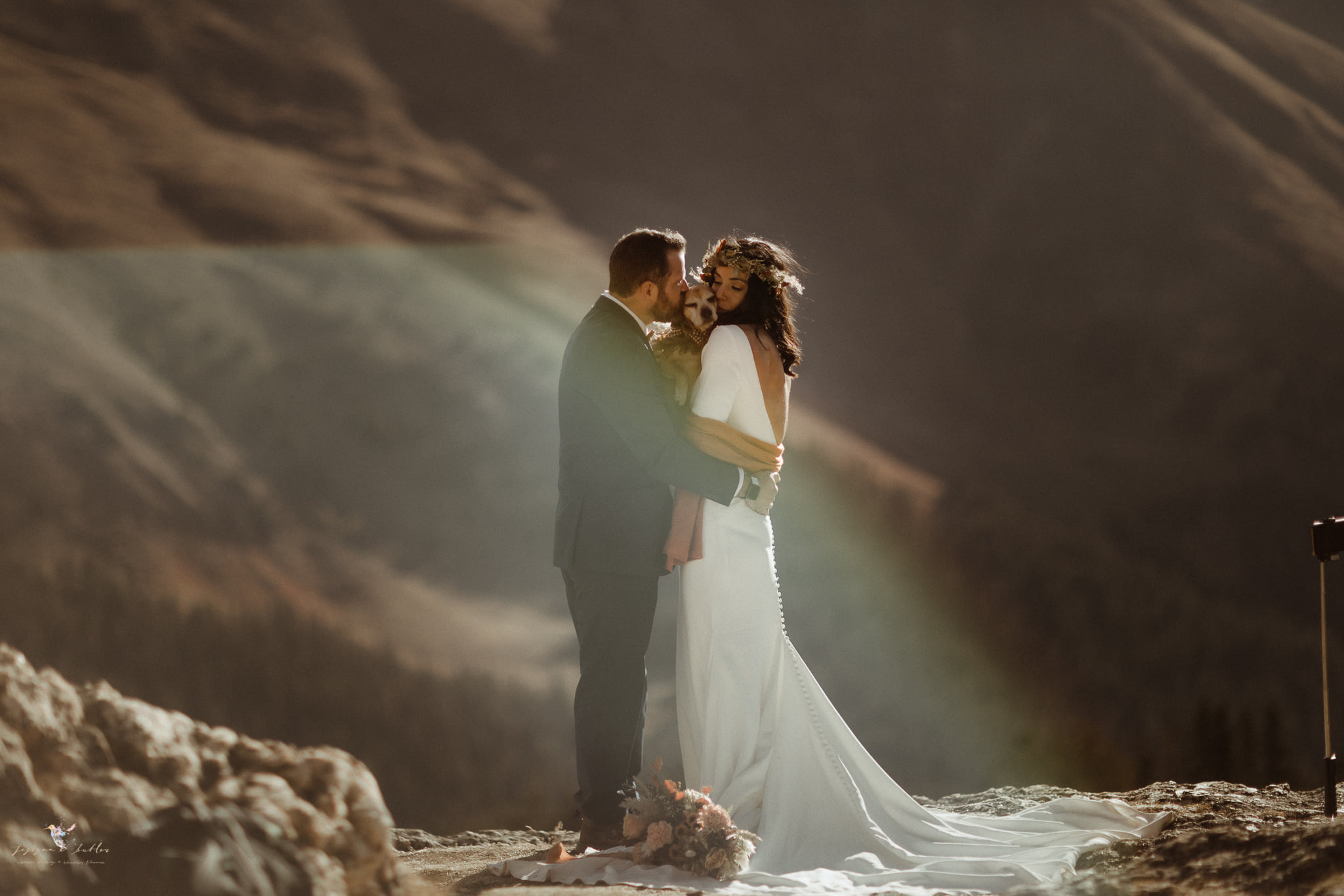 A wedding couple is holding each other and standing on a mountain top.