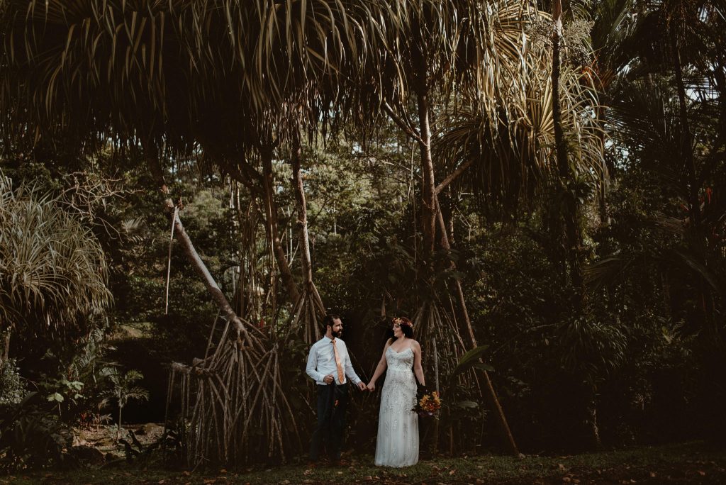 A wedding couple is holing hands in front of the rainforest in Costa Rica, captured by a destination wedding photographers.