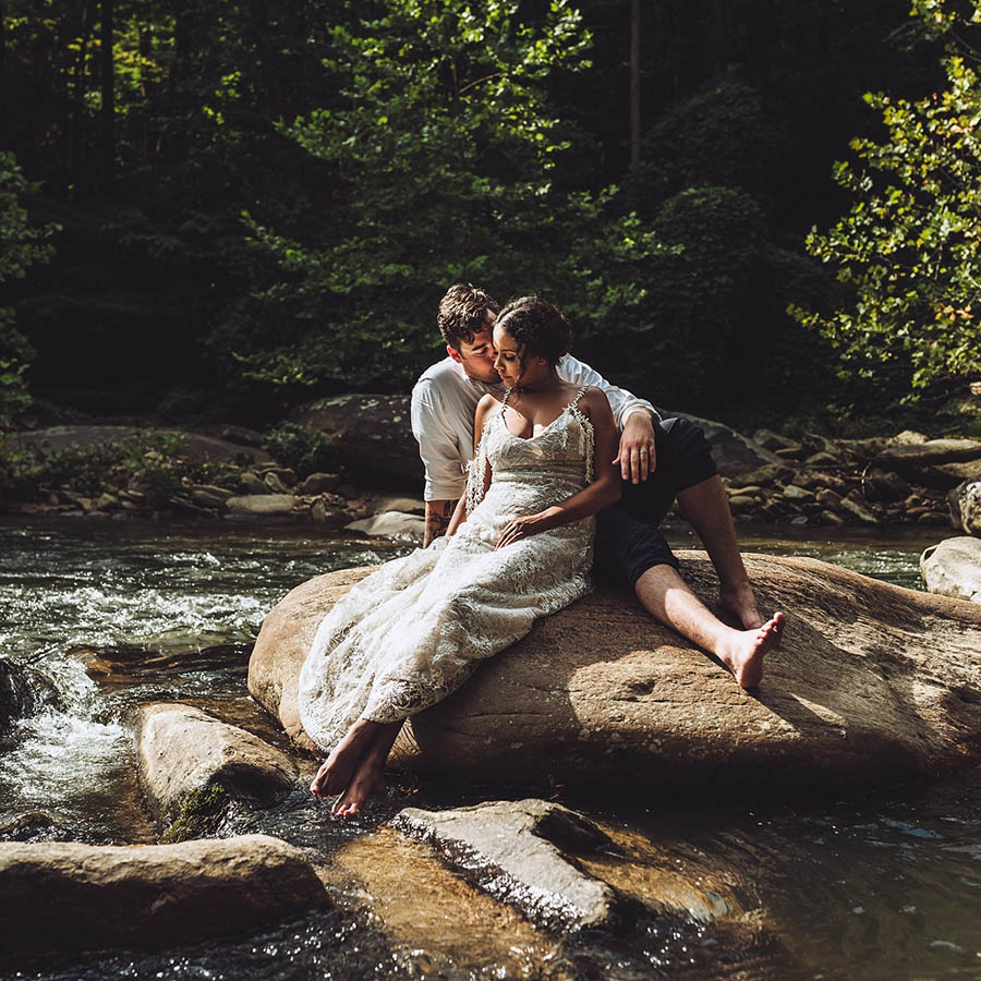 A wedding couple is sitting on a stone in a river in Asheville.