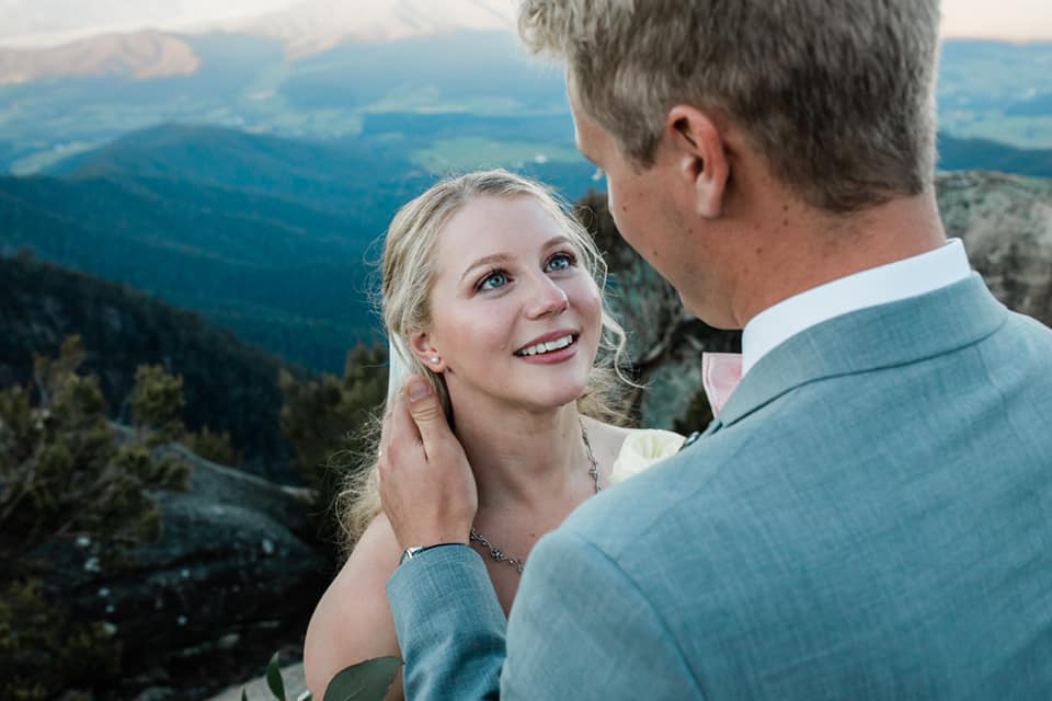 A wedding couple is standing on a mountain at looking at each other.