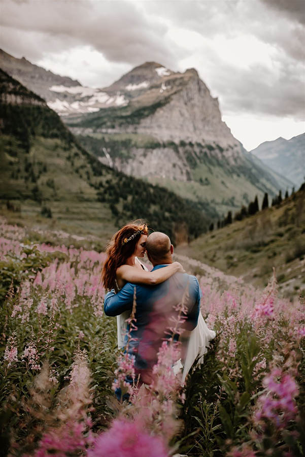 A groom is carrying his wife through a field of pink flowers in the Glacier National Park in Montana.