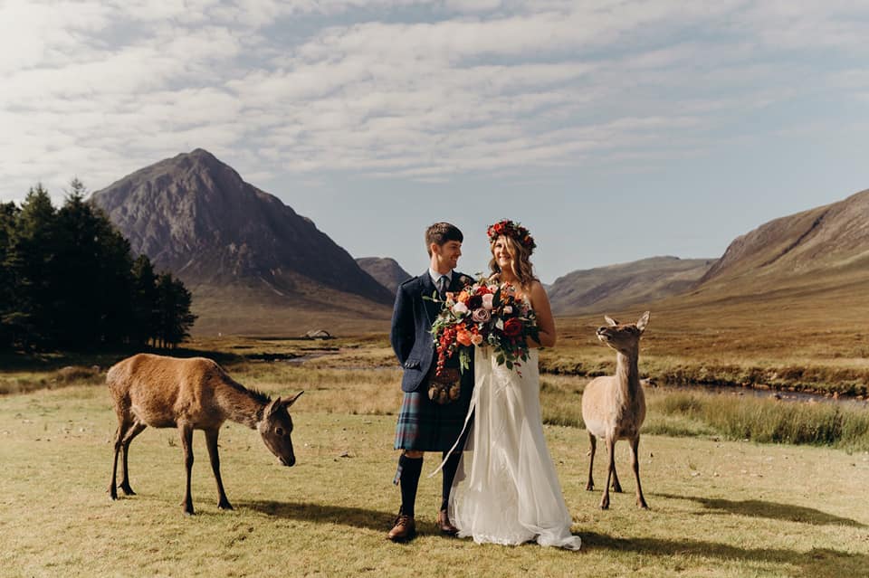 A wedding couple is standing in a valley next to goats in Glencoe.
