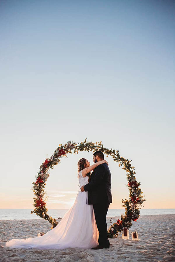 A wedding couple is holding each other and standing at the Panama City Beach in Florida.