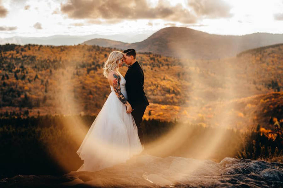 A wedding couple is standing on a flat rock and touching their foreheads and standing near a forest at the Black Balsam Knob.