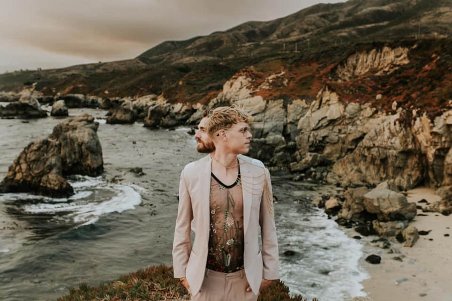 A wedding couple ist staining behind each other elevated on a mountain and in the background is the ocean and rocks located at the Big Sur.