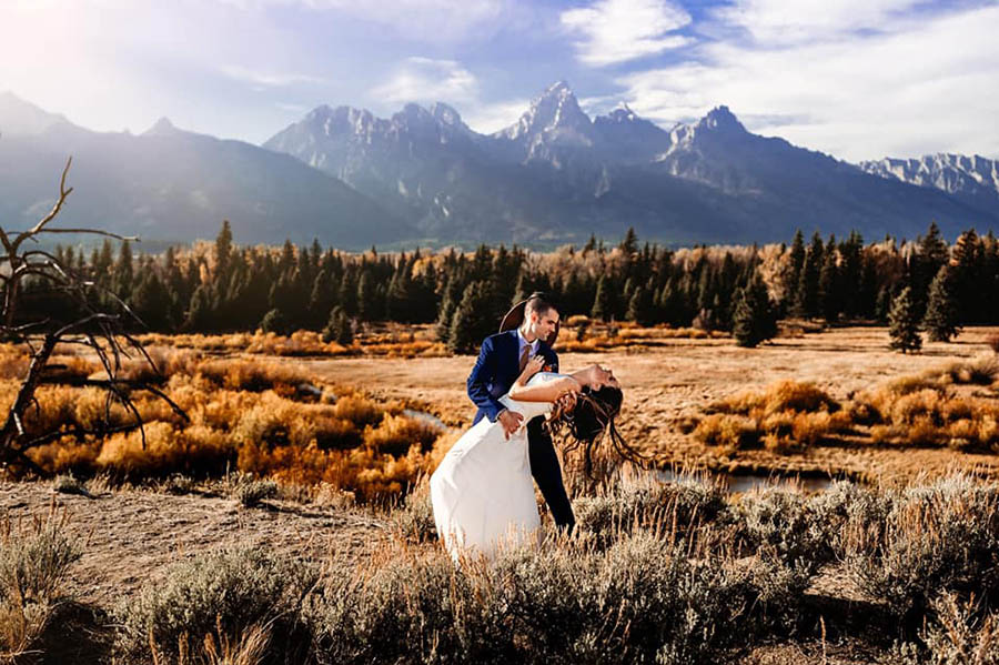 A groom is holding his bride and she is bending backwards and leaning into his arm and they are standing at the Grand Teton National Park.