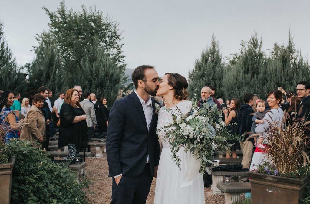 A wedding couple is kissing each other at the Hillside Gardens & Event Center, one of the wedding venues Colorado Springs offers.