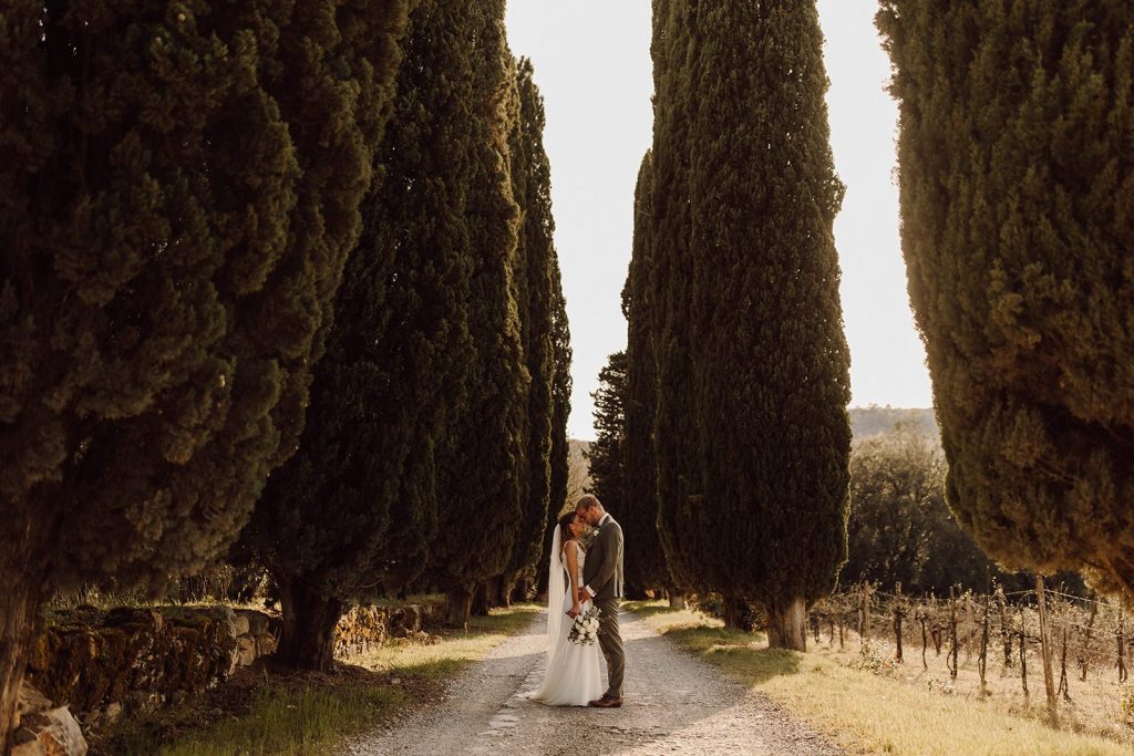A couple kissing in an ally of cypress trees during their Italy destination wedding