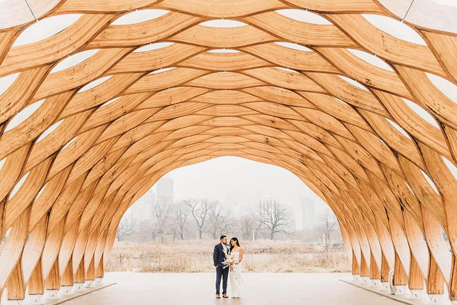 A wedding couple is standing in the middle of a wooden comb-shaped architectural structure in Chicago.