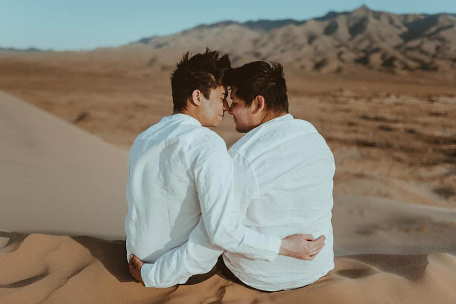 A wedding couple is facing each other and touching foreheads and are sitting in the Mojave Desert.