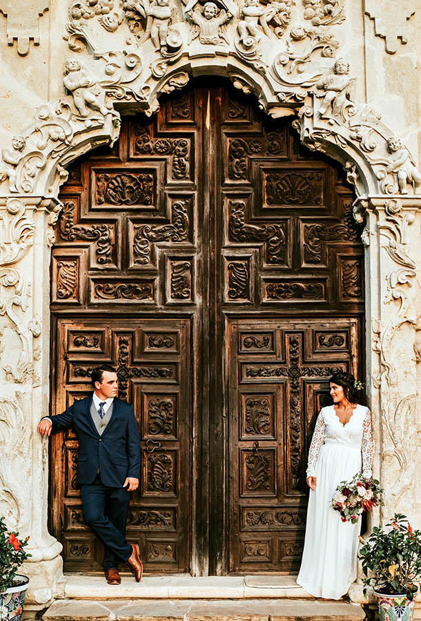 A wedding couple is standing in front of a huge wooden door in San Antonio.