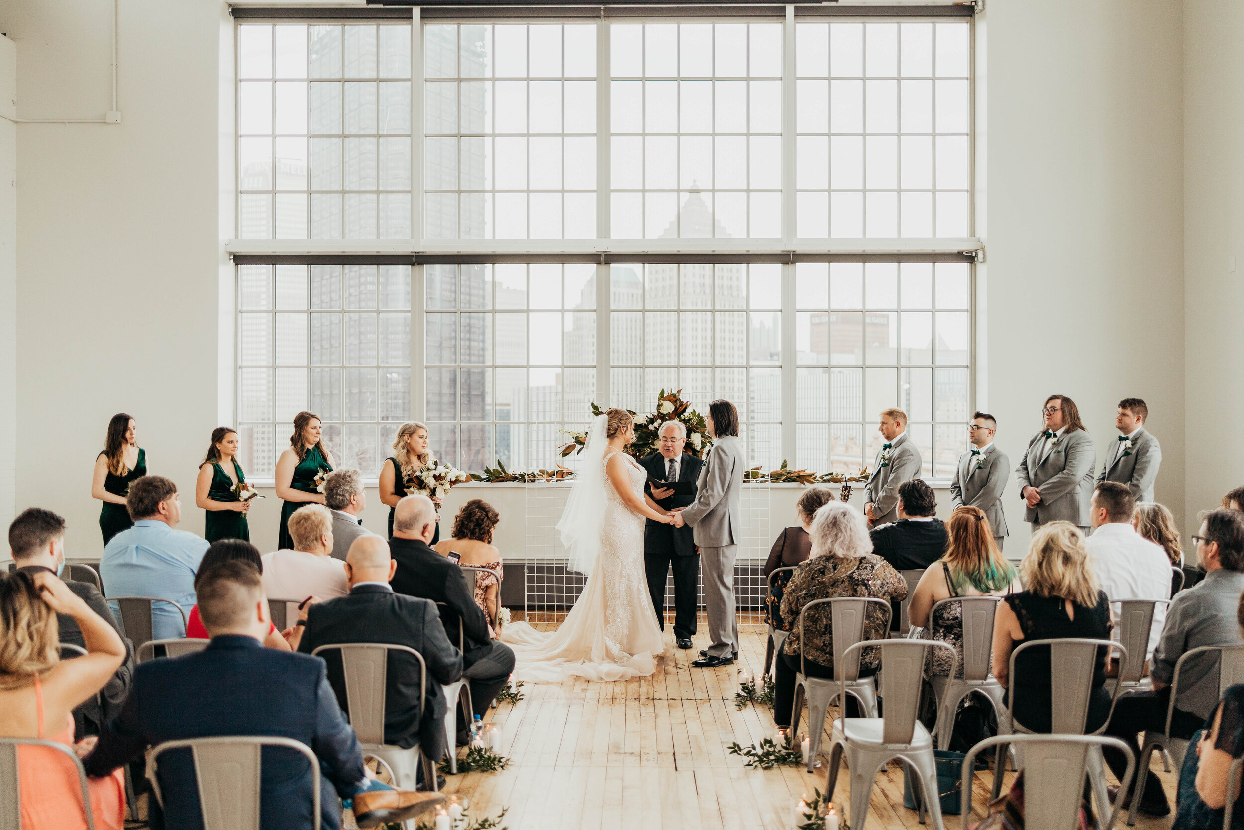 A wedding couple is getting married and standing in front of big industrial windows at the Energy Innovation Center in Pittsburgh.