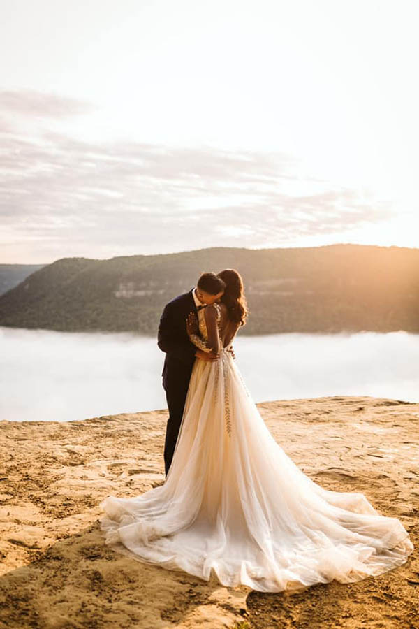 A groom is kissing his wife on her neck whilst and the couple is standing on a sandy plateau at the Signal Mountain in Tennessee.