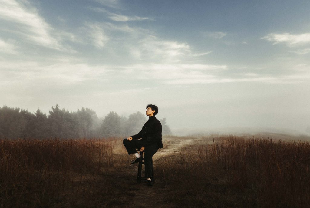 a black woman is sitting on a barstool in a field on a cloudy day