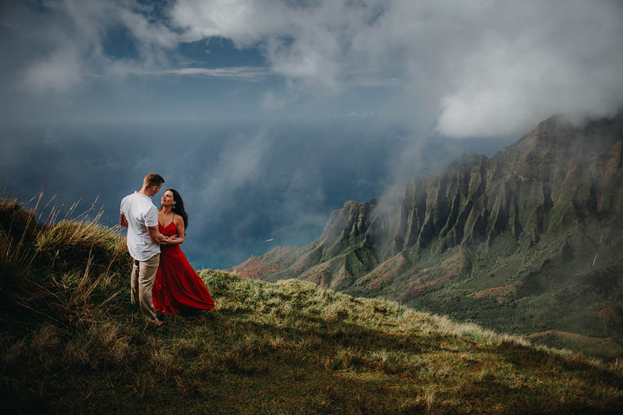 A couple is holding each other and looking at each other whilst standing on a field of grass on a mountain in Kauai.