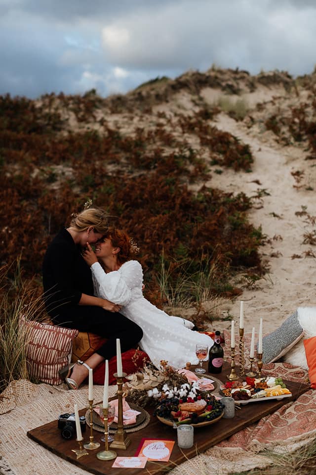 A wedding couple is kissing each other an sitting on a blanket on the beach near Jersey.
