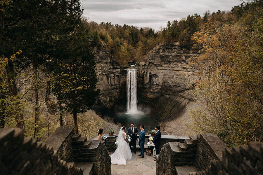 A wedding couple is standing in front of the Taughnnock Falls and getting married. 