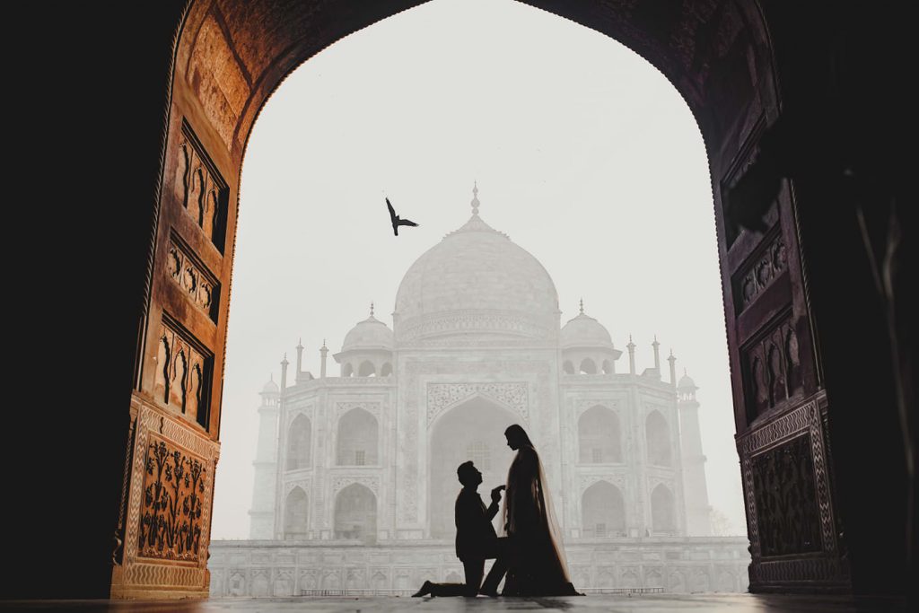 Silhouette of a couple in a marriage proposal moment at the Taj Mahal, framed by a grand arched entrance, highlighting engagement photography guide