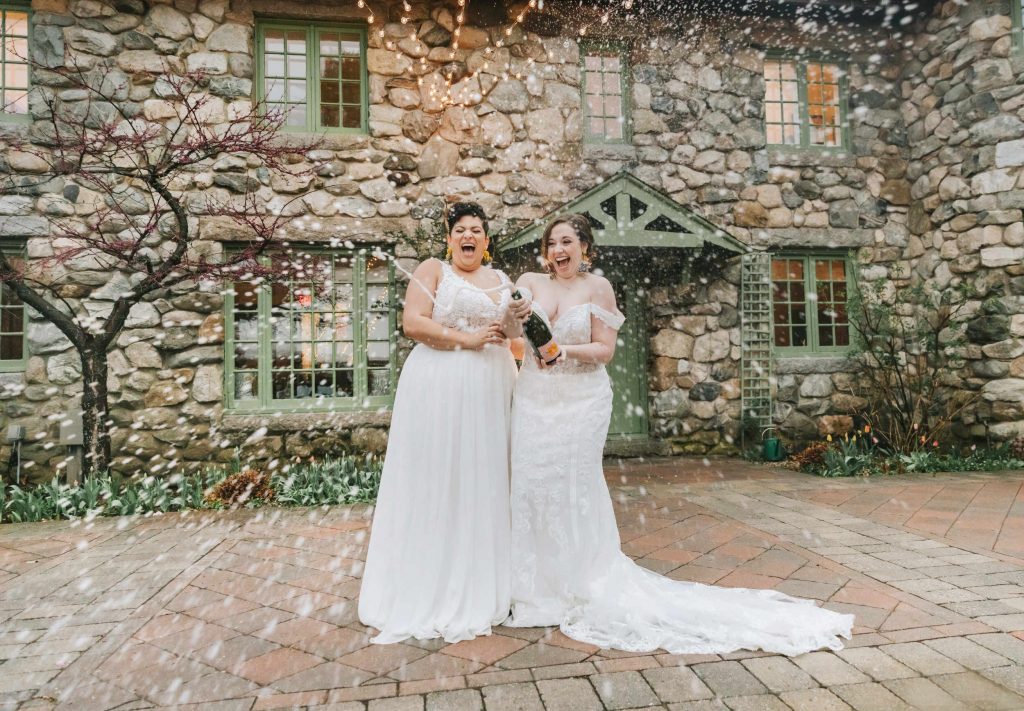 A wedding couple is opening up bottles of champaign at the Willowdale Estate, one of the Boston wedding venues.