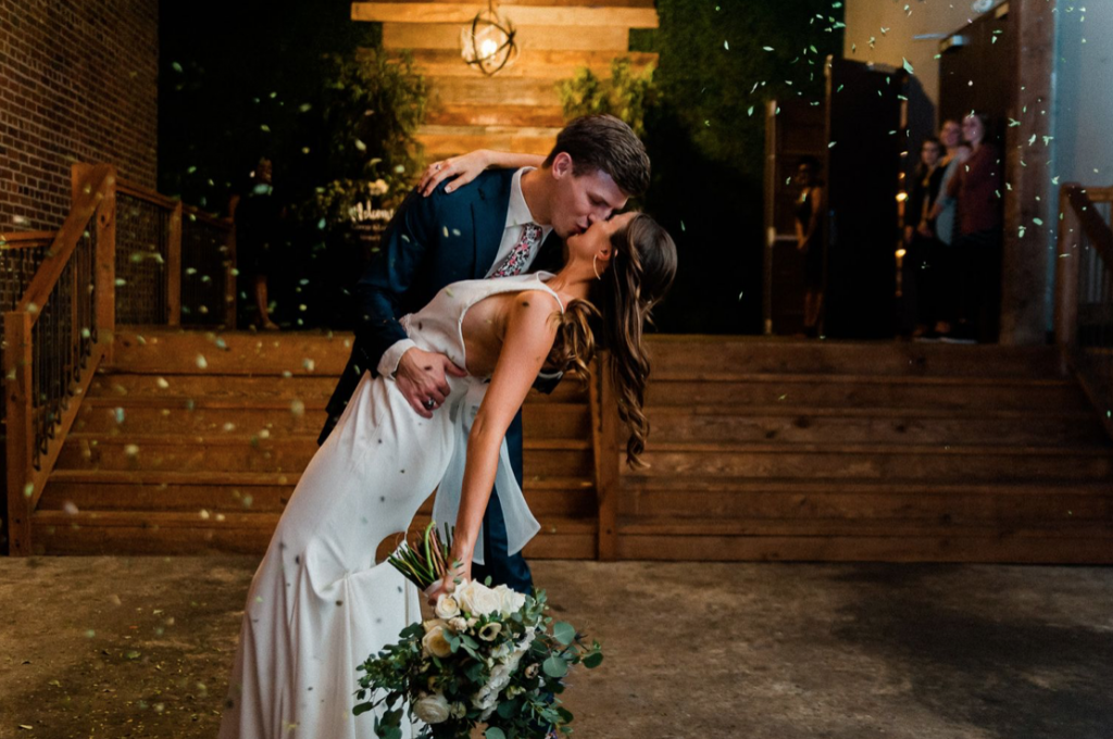 A wedding couple is kissing each other path the Loft 212, one of the wedding venues in Alabama.