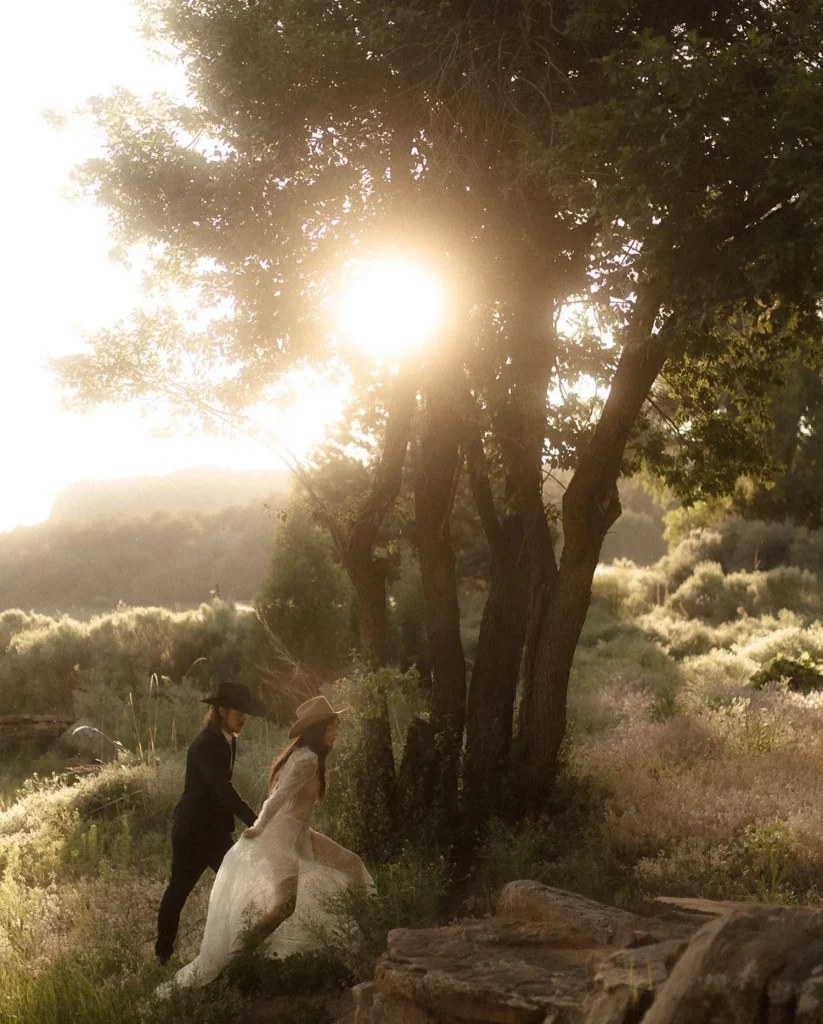 A joyful bride and groom in elegant wedding attire running hand in hand through a sunlit grove, with the sun casting a radiant glow through the trees, creating a magical atmosphere for their special day.