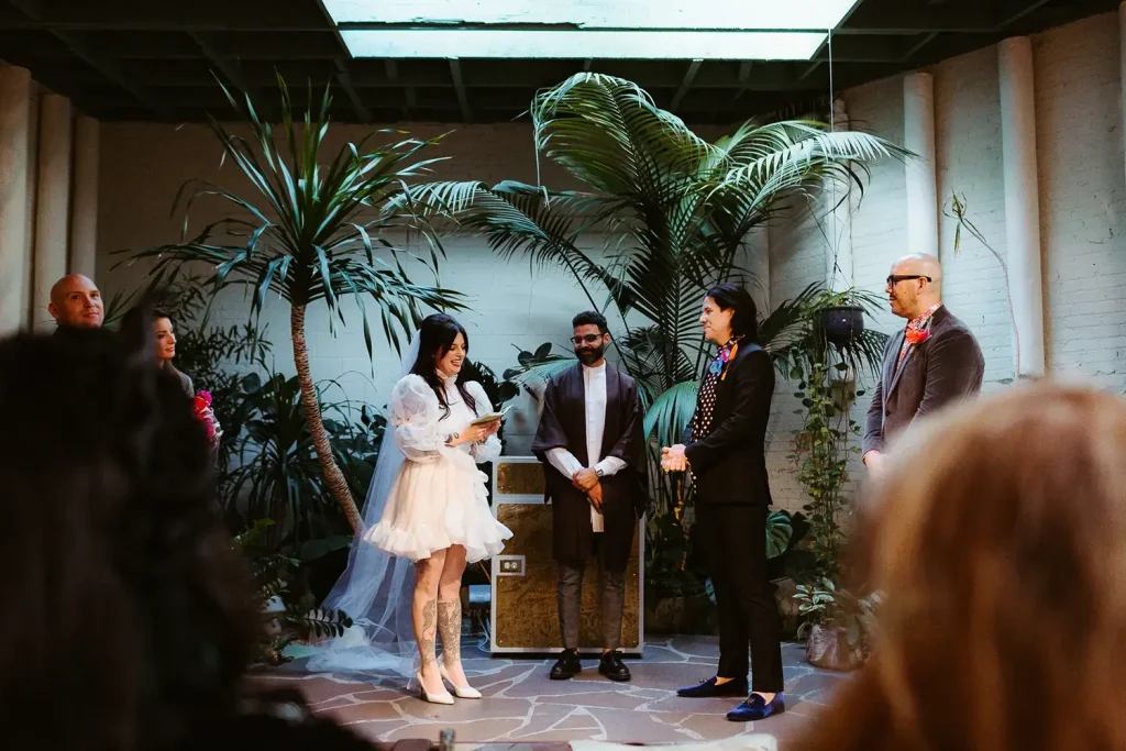 A wedding ceremony takes place in a lush, indoor venue with tropical plants, as the bride reads her vows to the groom. This captivating scene showcases the intimate and vibrant moments perfect for marketing your wedding photography business.