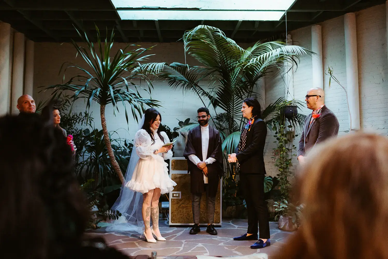 A wedding ceremony takes place in a lush, indoor venue with tropical plants, as the bride reads her vows to the groom. This captivating scene showcases the intimate and vibrant moments perfect for marketing your wedding photography business.