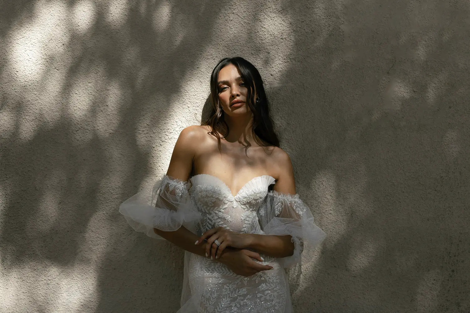 Bride in a detailed lace wedding dress standing against a textured wall, highlighting the natural light effects enhanced by Essence Editorial Wedding Presets.