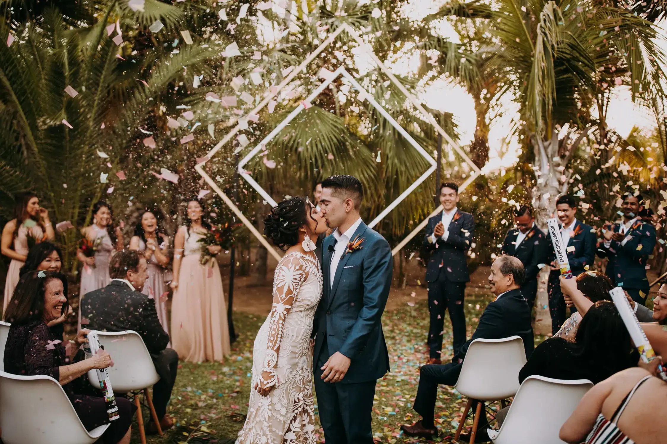 Newlyweds kiss amid confetti at Acre Resort, one of the popular destination wedding venues in Mexico, surrounded by joyous guests and lush palm trees.