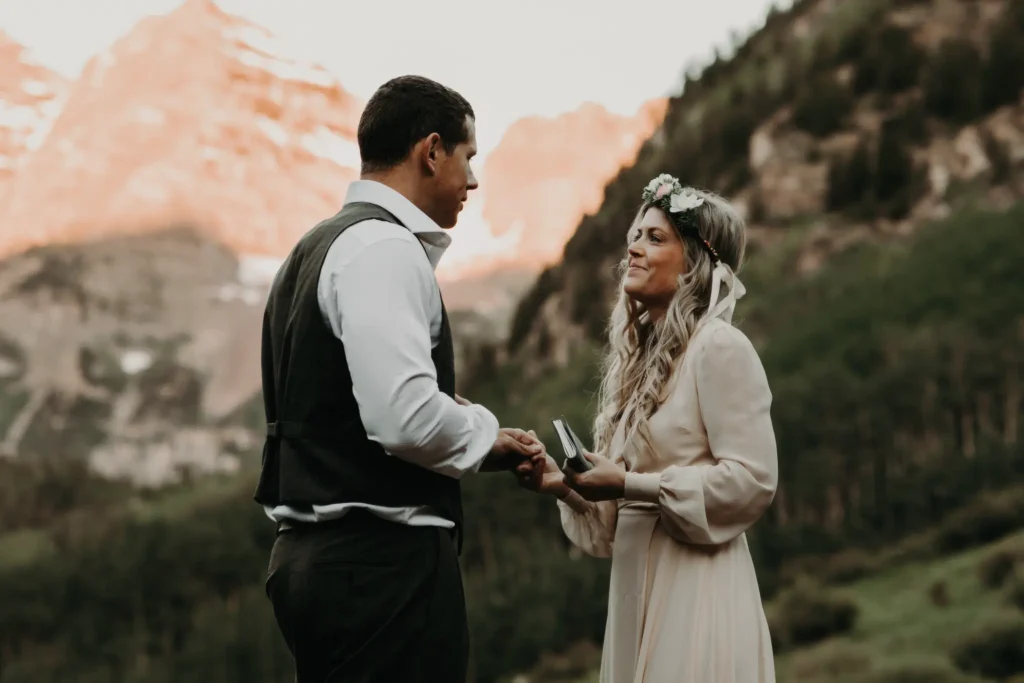 A couple exchanged vows during an elopement and booked Elopement packages in Colorado. The ceremony is in the scenic mountains of Colorado, with the groom wearing a vest and the bride in a long-sleeved dress and floral crown.