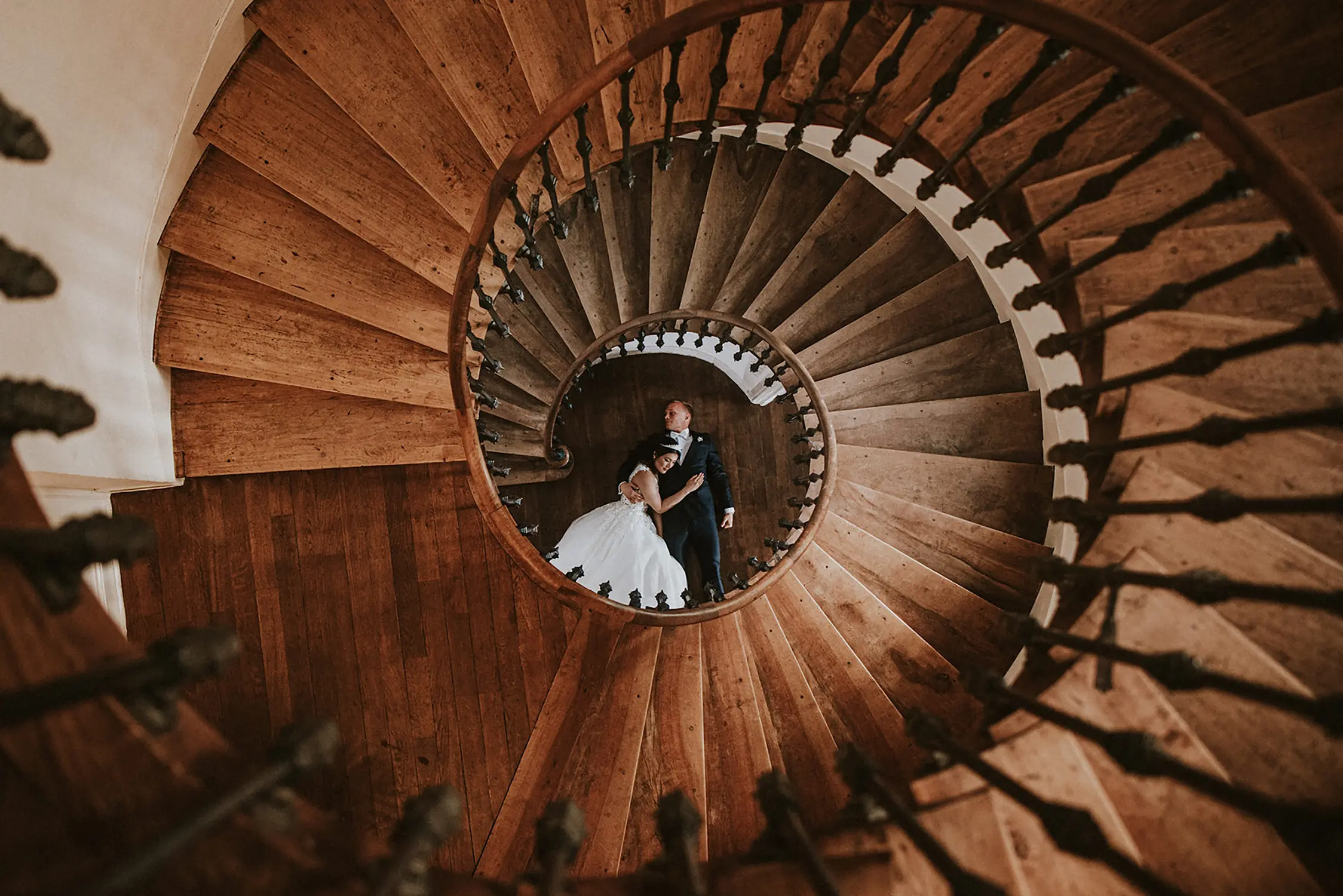 Overhead shot of newlyweds embracing at the bottom of a spiral staircase, showcasing the use of creative perspectives in wedding photography for social media appeal.