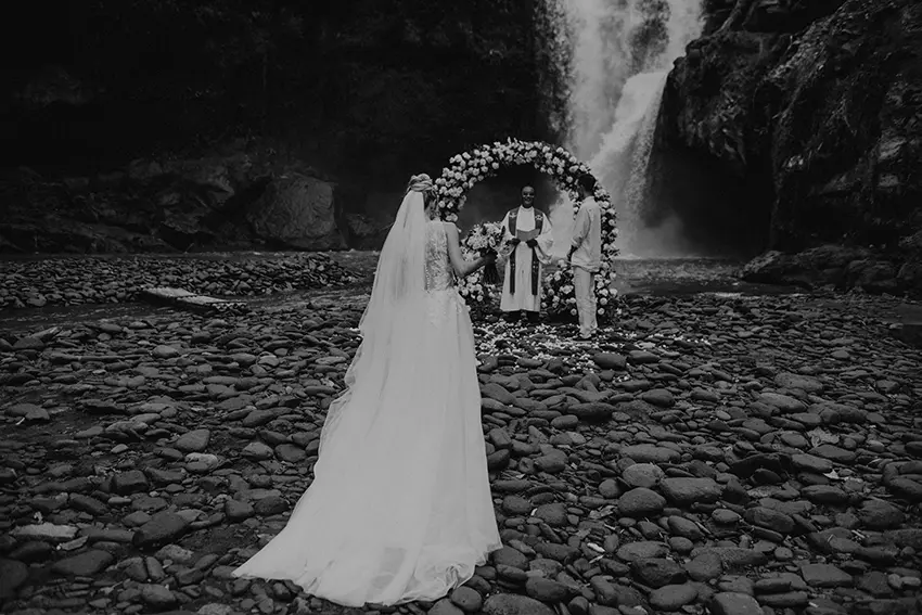 Bride and groom exchanging vows under a floral arch in front of a waterfall, exemplifying elopement photography tips.